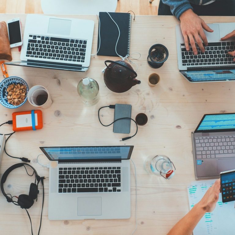 Two people working on laptops at a table with various office supplies and drinks.
