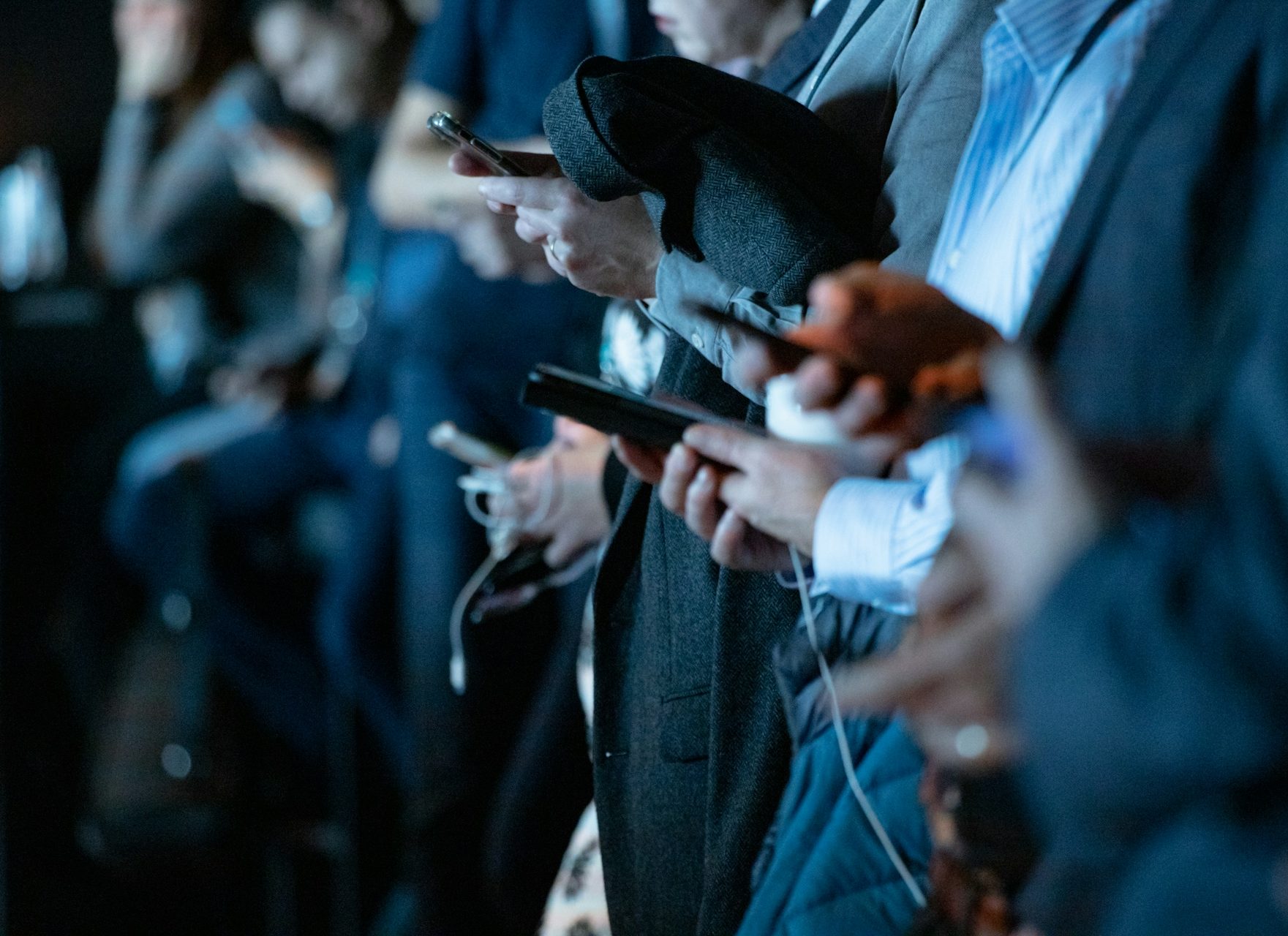 Hands holding smartphones, dressed in business attire, at an event or conference.