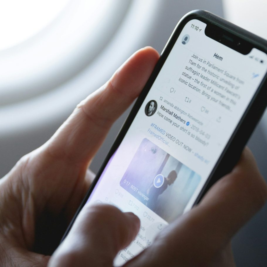 A hand holding a smartphone displaying a social media feed with a video.
