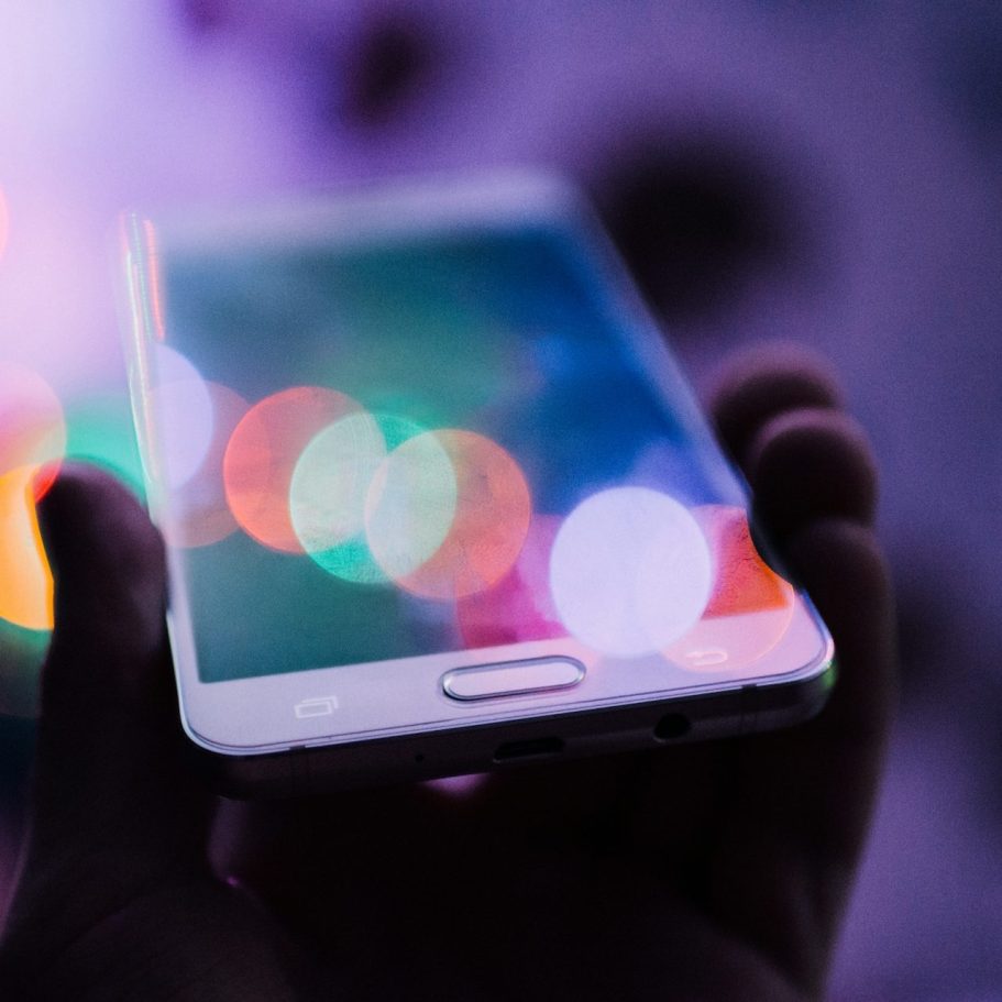 A hand holding a smartphone displaying colorful, blurred light bokeh.